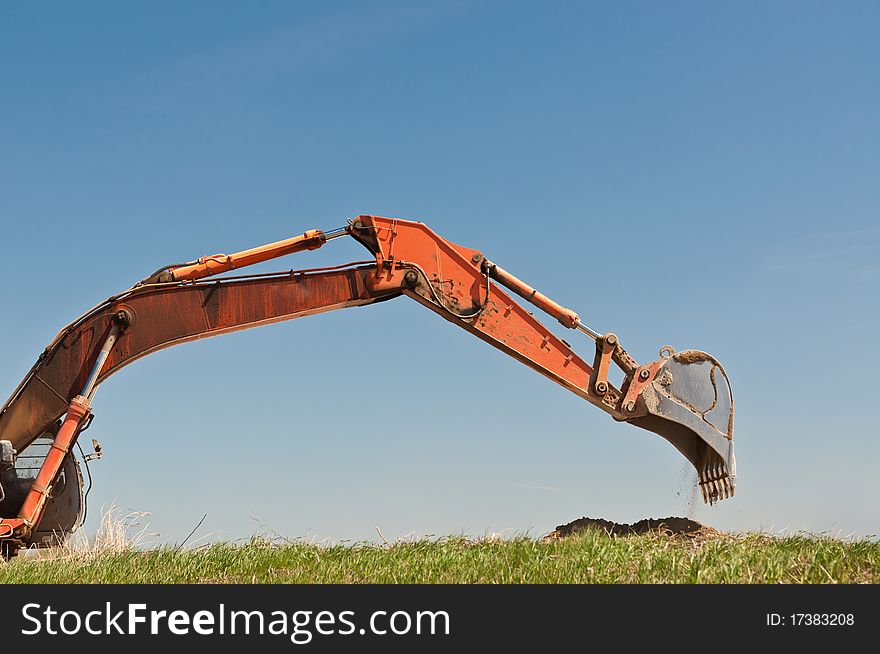 The arm and bucket of a hydraulic excavator that is digging into a grassy hillside. The arm and bucket of a hydraulic excavator that is digging into a grassy hillside.