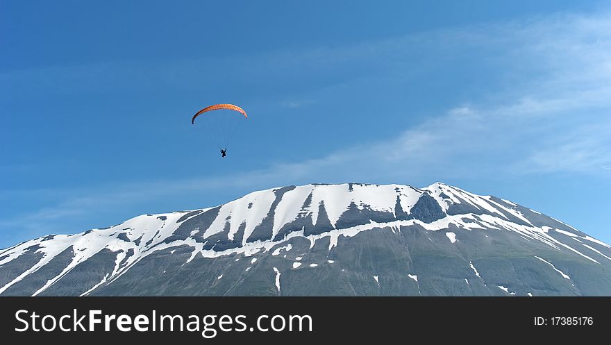 A paraglider soars over a snow-capped mountain. A paraglider soars over a snow-capped mountain