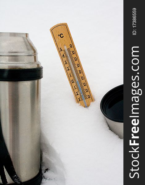 Thermometer in the snow and a thermos of tea. Thermometer in the snow and a thermos of tea