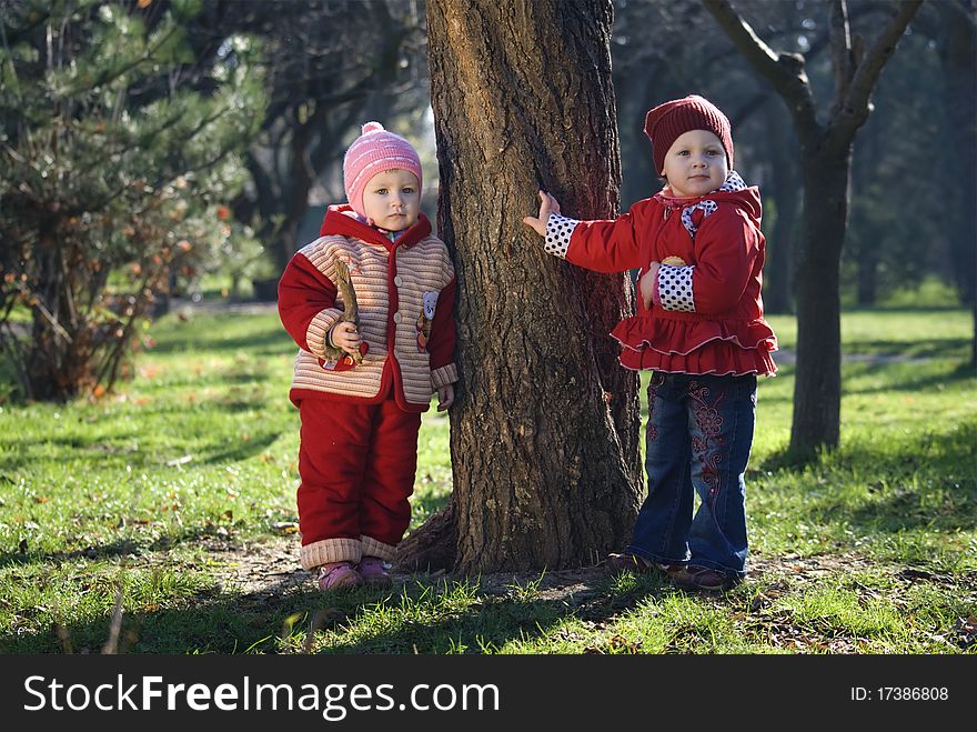 two little girls stand near a tree