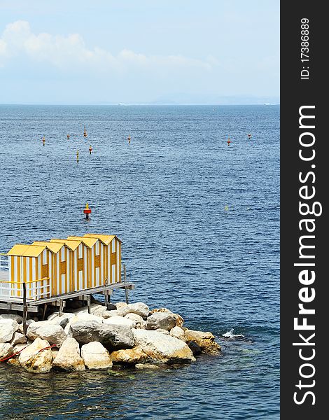 A row of yellow bath houses on a rocky wall next to the water.