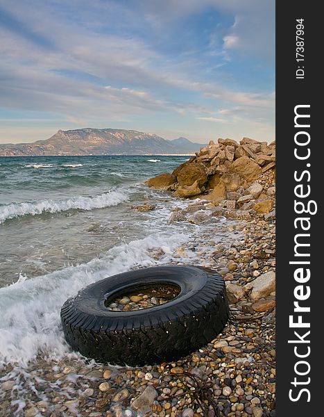 Pollution - Old tyre washed up on pebble Mediterranean beach. Pollution - Old tyre washed up on pebble Mediterranean beach