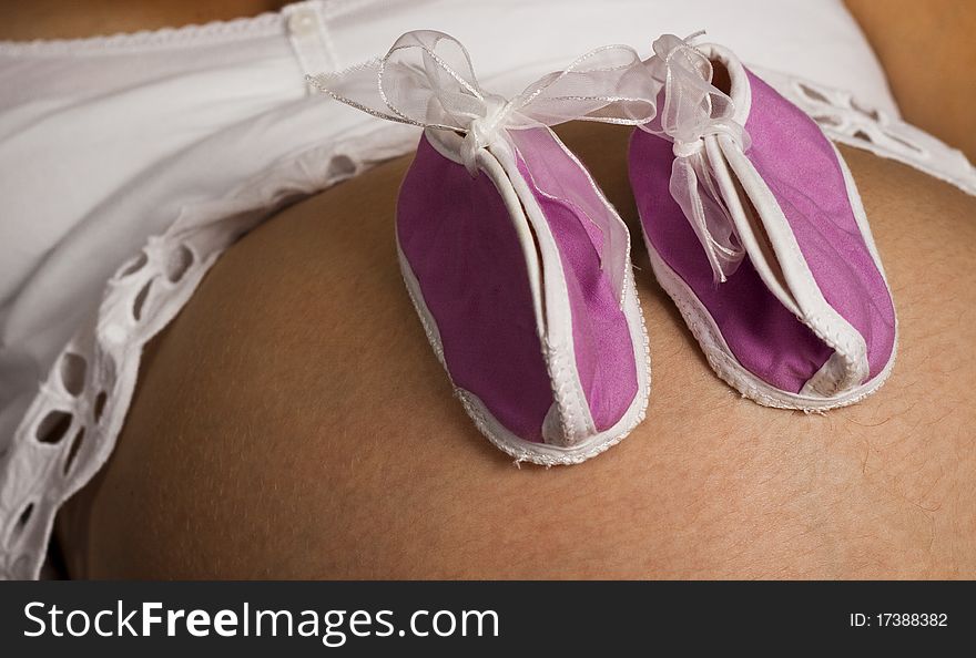 Pink baby shoes on a black and white pregnant belly
