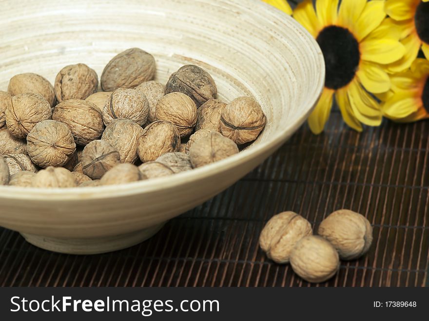 Wooden bowl with walnuts on mat. some blurred sunflowers.