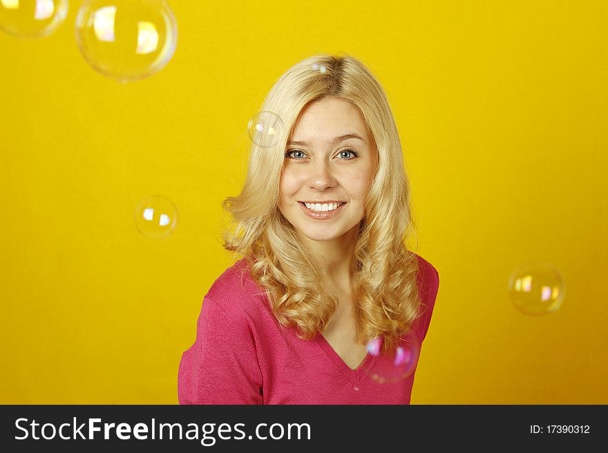 Young beautiful woman on a yellow background rejoices soap bubbles. Young beautiful woman on a yellow background rejoices soap bubbles