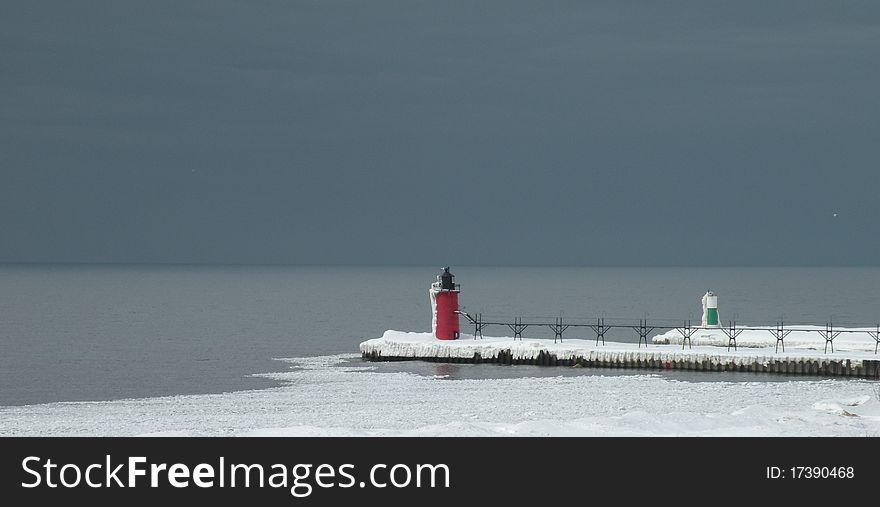 South Haven Michigan lighthouse frozen in time. Red lighthouse with pier extending to shore covered in snow and ice. Ominous sky as snow threatens. South Haven Michigan lighthouse frozen in time. Red lighthouse with pier extending to shore covered in snow and ice. Ominous sky as snow threatens.