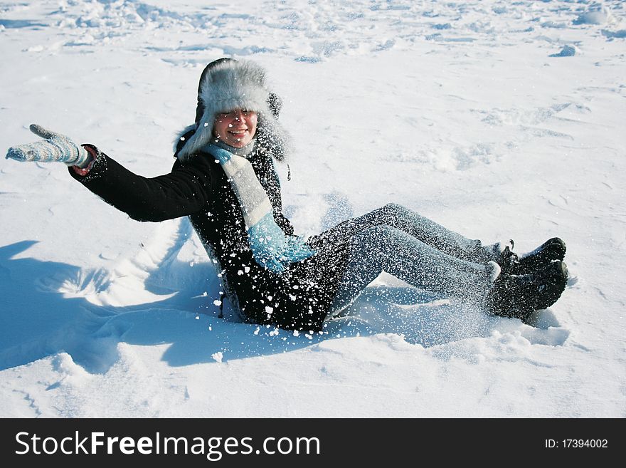 Smiling girl in cap with ear-flaps laying on the snow