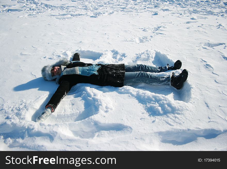 Smiling girl in cap with ear-flaps laying on the snow