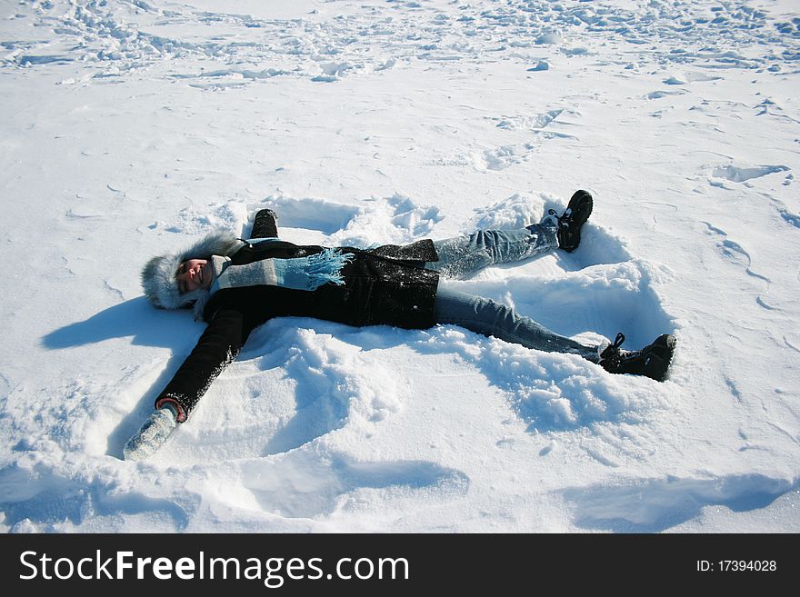 Smiling girl in cap with ear-flaps laying on the snow
