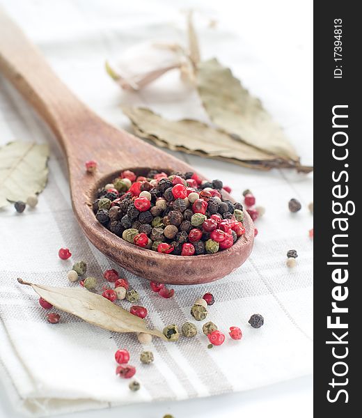 Peppercorns in wooden spoon with garlic on background