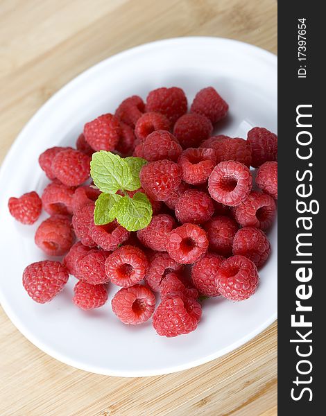 Ripe fresh raspberries on a small white round plate and bamboo background. Ripe fresh raspberries on a small white round plate and bamboo background.