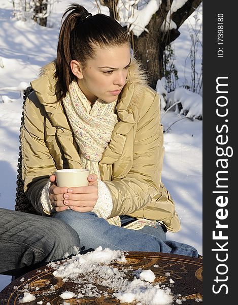 White woman drinking tea outside, trees with snow on branches in background. White woman drinking tea outside, trees with snow on branches in background