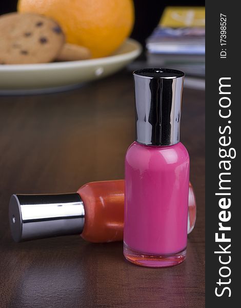 Nail polish placed on a table in front of a stack of magazines and a plate with food.