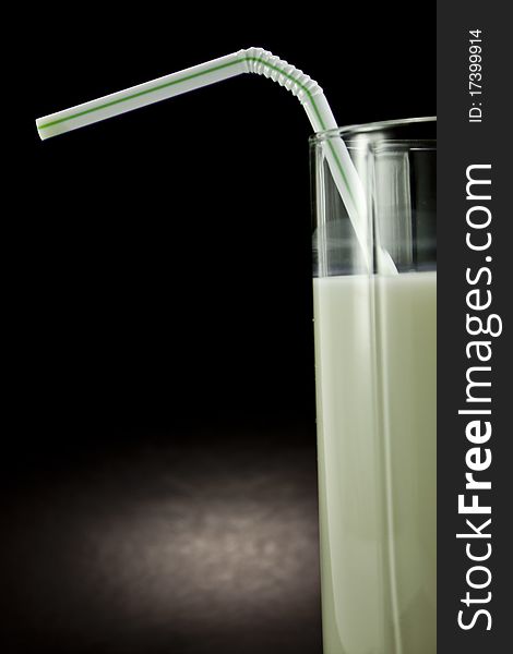 Milk in a glass on a black background with a straw. Milk in a glass on a black background with a straw