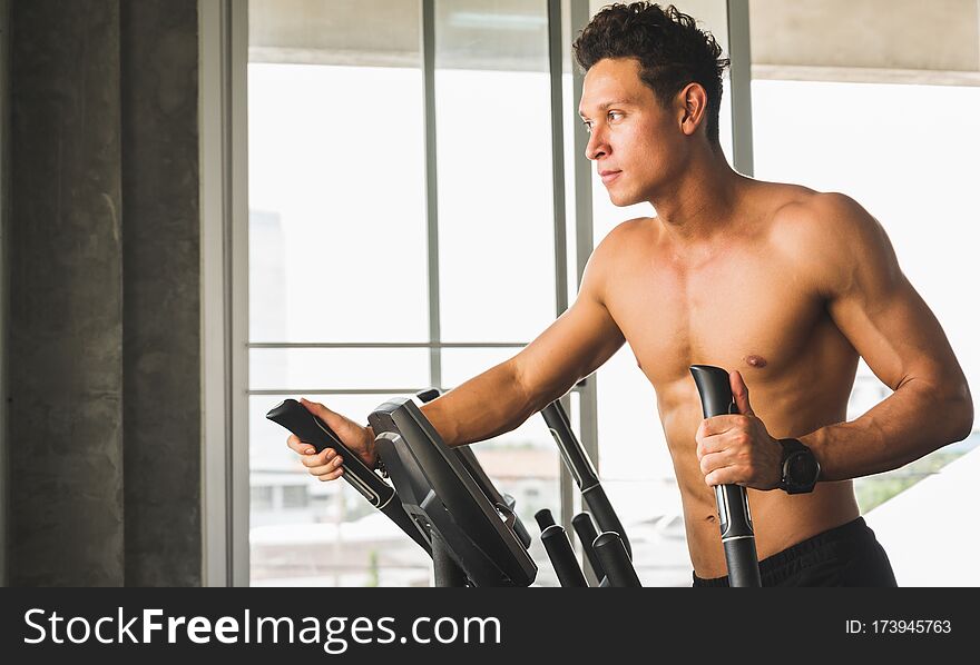Young Man At The Gym Exercising On The Cross Trainer Machine. Fitness Man Doing Cardio Workout Program