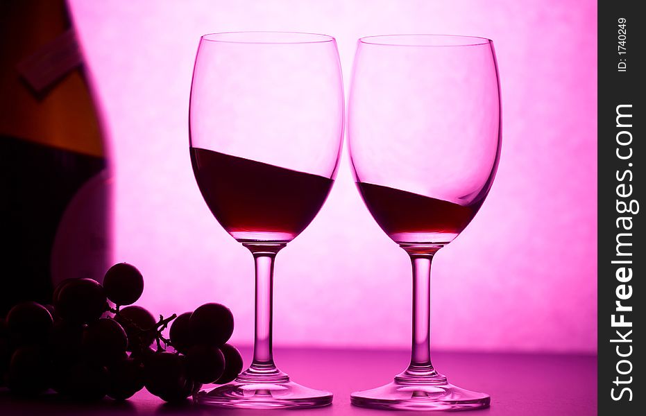 Two wineglasses with some grape in pink light. Two wineglasses with some grape in pink light