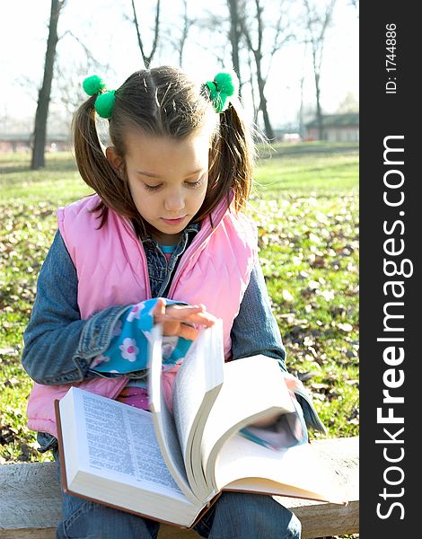 Little pretty child reading the book in the park