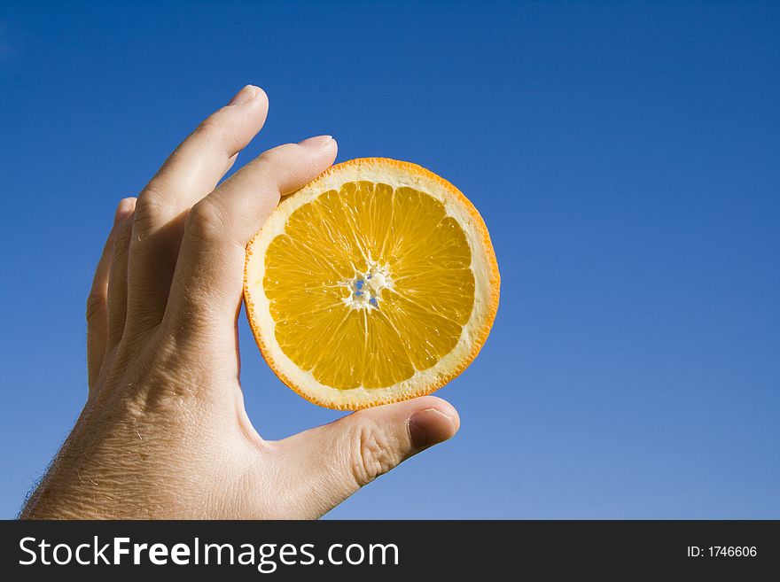 Hand holding an orange slice against clear blue sky background. Hand holding an orange slice against clear blue sky background