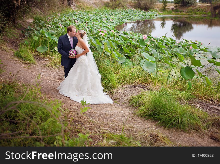 Kissing bride and groom near lotos pond