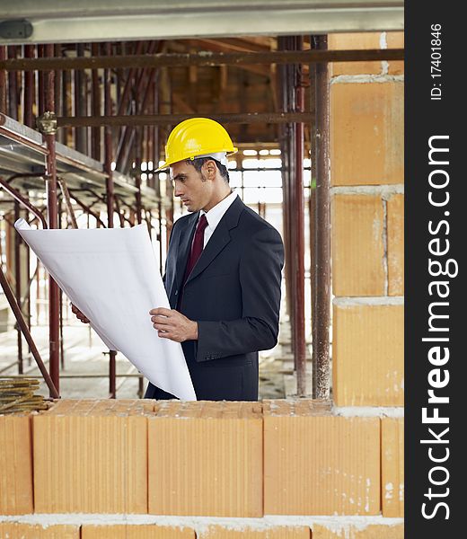 Caucasian male architect holding blueprints near brick wall. Vertical shape, waist up, side view, copy space. Caucasian male architect holding blueprints near brick wall. Vertical shape, waist up, side view, copy space