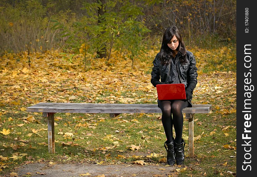 Beautiful young girl with red laptop in autumn park. Beautiful young girl with red laptop in autumn park