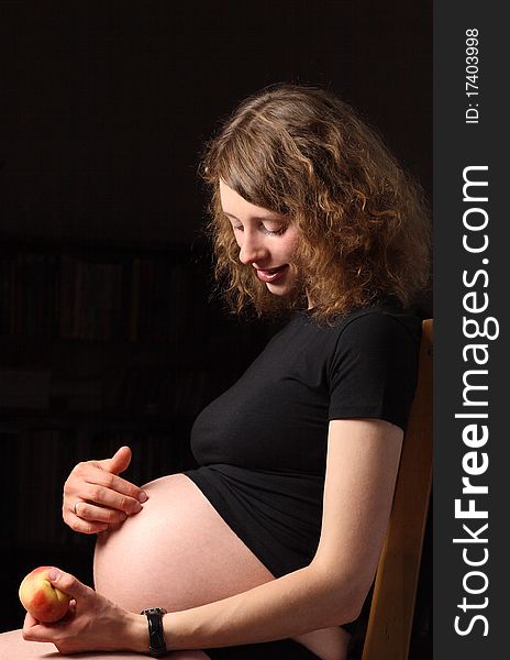 Smiling young pregnant woman with peach sitting on the chair. Smiling young pregnant woman with peach sitting on the chair