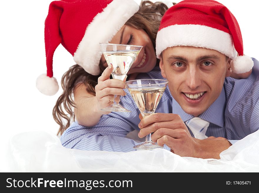 Young lovely couple in Santa hats holding the glasses of champagne and clinking glasses. Isolated over white background. (Focus is on champagne glasses). Young lovely couple in Santa hats holding the glasses of champagne and clinking glasses. Isolated over white background. (Focus is on champagne glasses)
