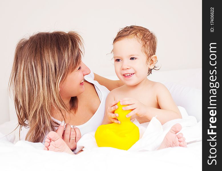 Young beautiful mother and her baby on the bed at home after the shower