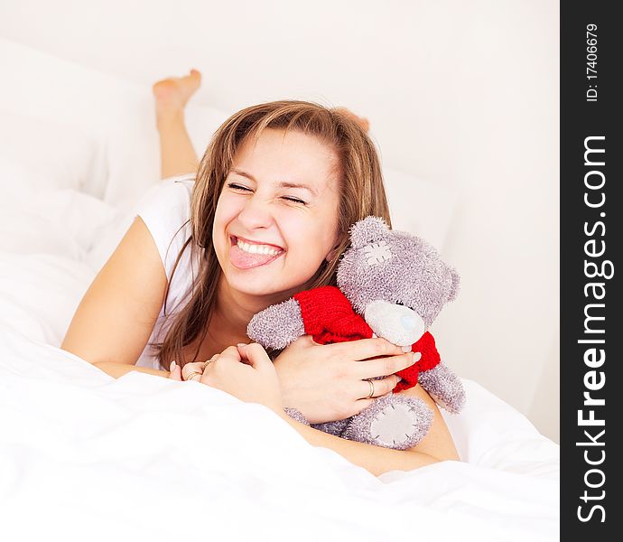 Young blond woman with a toy bear on the bed at home. Young blond woman with a toy bear on the bed at home