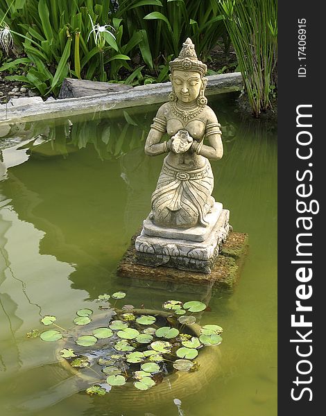 Female ornamental statue kneeling on pedistal in pond, Thailand