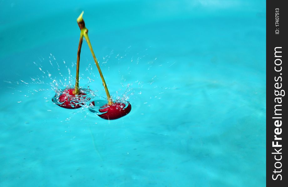 An image of cherry fruti droping into water against blue background. An image of cherry fruti droping into water against blue background