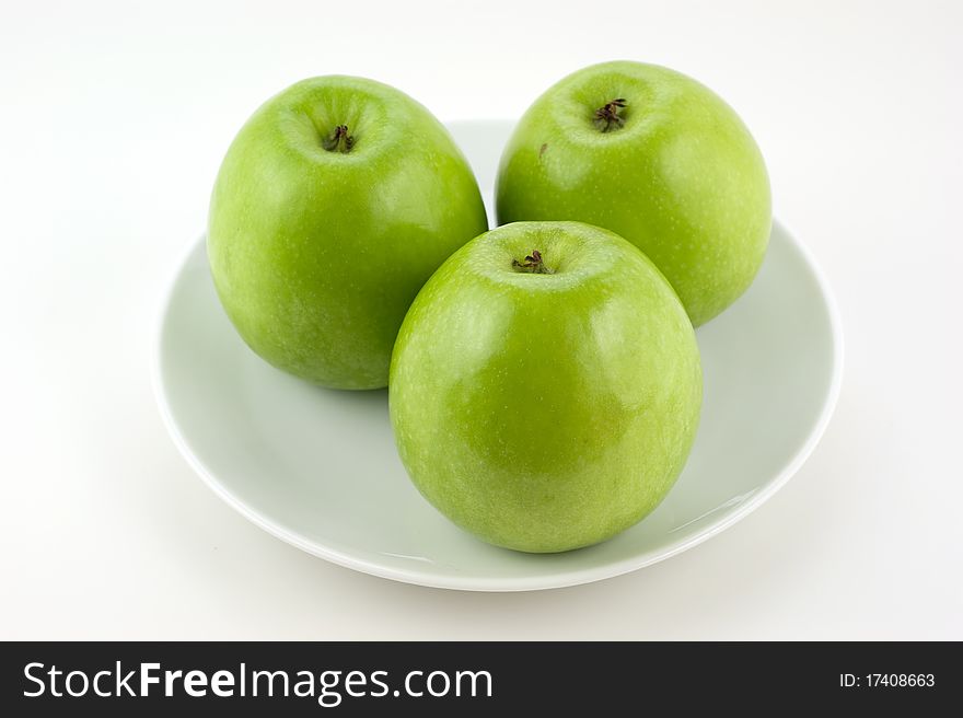 Three green apples on plate on a white background closeup