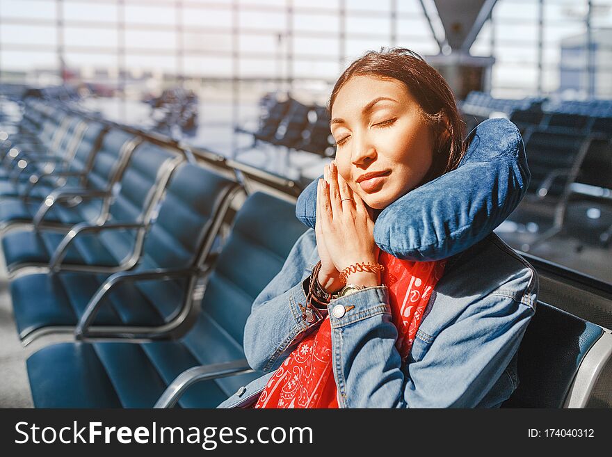 Woman relaxing and sleeping with neck pillow at airport terminal awaiting the delayed flight, transportation and travel concept