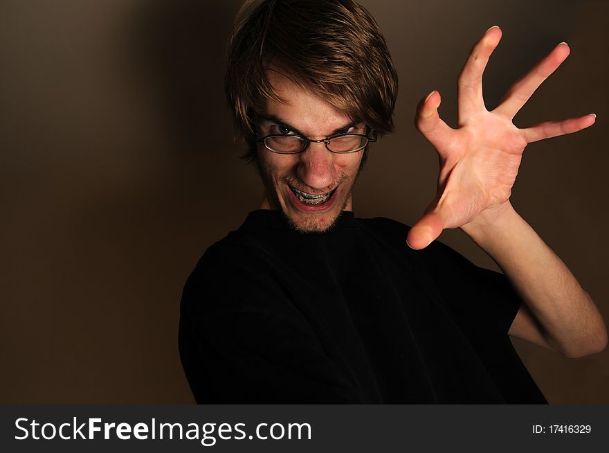 Young man ready to grab, touch, or something with his large hand claw. He looks like a techie with his glasses and braces on, but can qualify as any sort of regular person being scary. Young man ready to grab, touch, or something with his large hand claw. He looks like a techie with his glasses and braces on, but can qualify as any sort of regular person being scary.