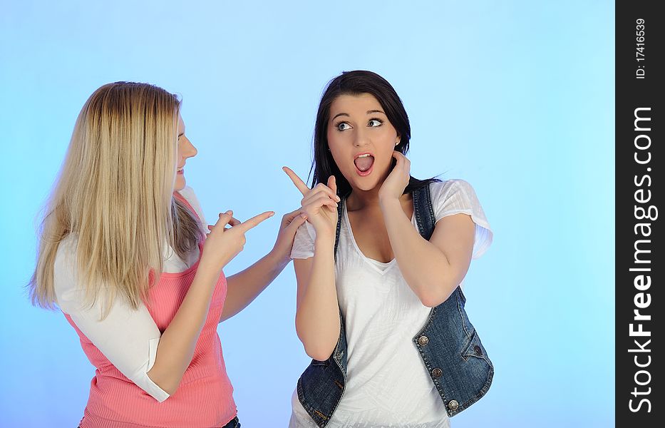 Two young pretty woman gossiping and enjoying conversation. isolated on blue background