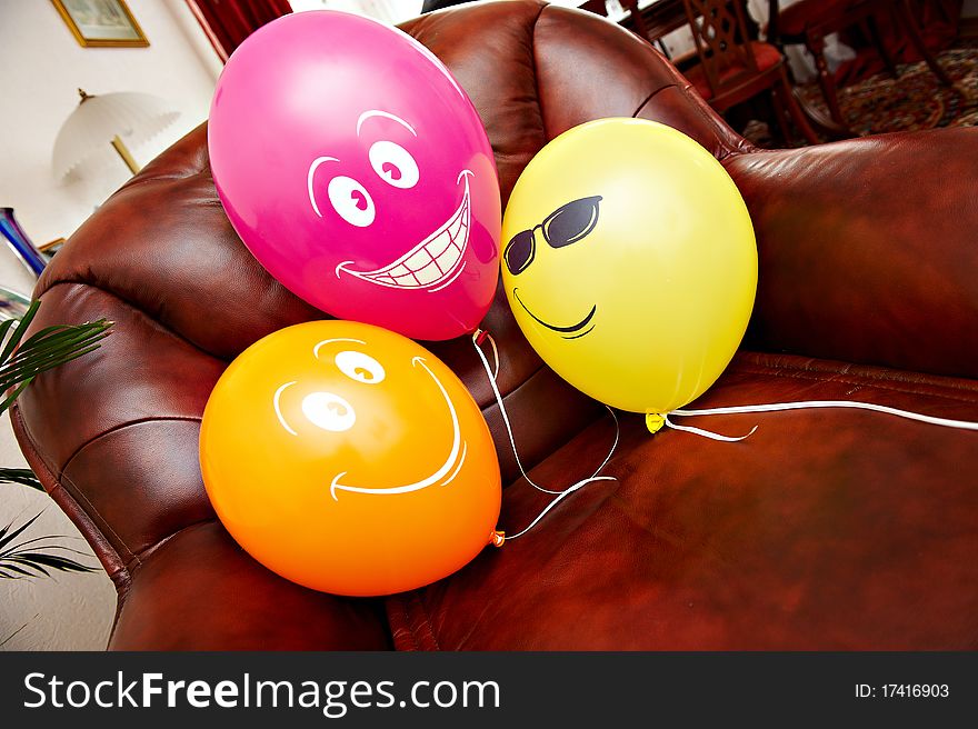 Three fanny red yellow and orange balloons on brown leather chair. Three fanny red yellow and orange balloons on brown leather chair