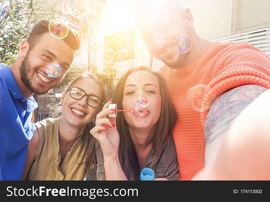 Happy friends taking snapshot selfie with mobile phone while throwing soap bubbles in camera - Young people having fun with new trends technology - Main focus on right women eyes and near men face