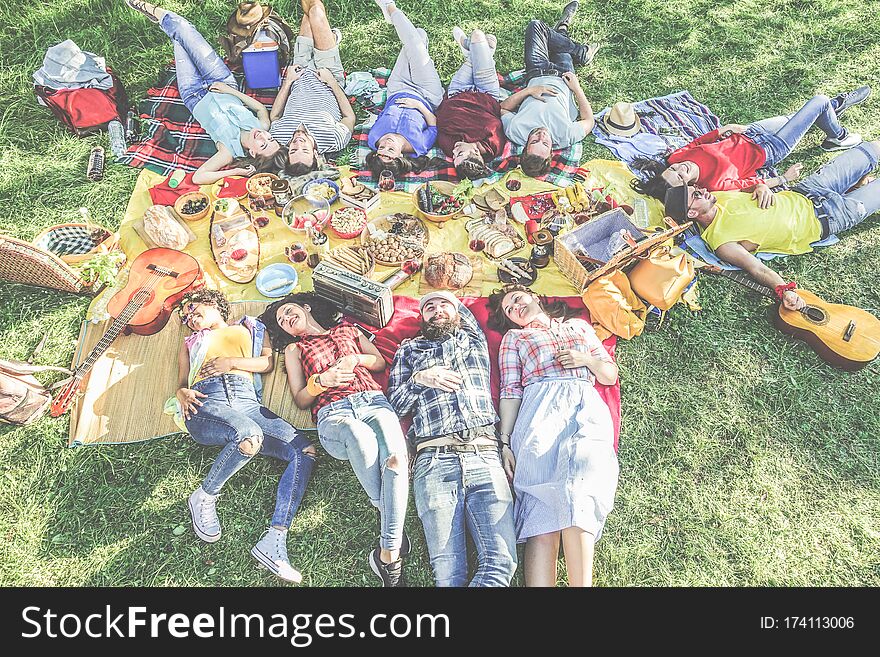 Happy friends lying down at picnic with barbecue on city park outdoor - Young people eating enjoying time together in summer time - Focus on bottom guys