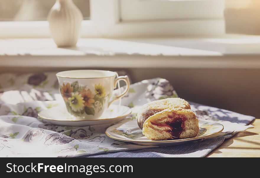 Selective focus of home made jam doughnuts with burry background of cup of hot blueberry tea, Soft focus of afternoon tea served with strawberry jam donut in sunny day summer, English traditional