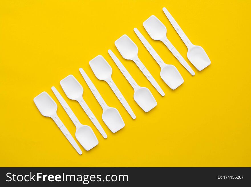 White Plastic Spoons On Yellow Background. Fast Food, Eco And No Plastic Concept. Top View. Copy, Empty Space For Text