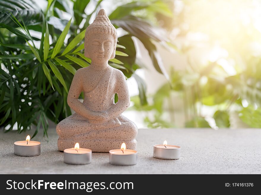 Natural stone statue of Buddha sitting in meditation surrounded by candles and tropical plants