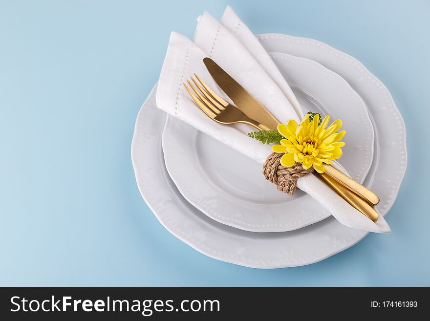 Spring or Easter table setting with golden cutlery white dishes yellow daisy flower on blue table copy space top view. Spring or Easter table setting with golden cutlery white dishes yellow daisy flower on blue table copy space top view