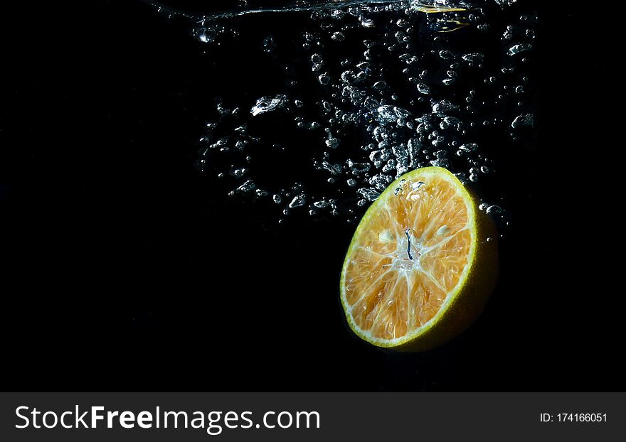 Oranges fall into the water until the sponge splits beautifully on a black background. Summer drink