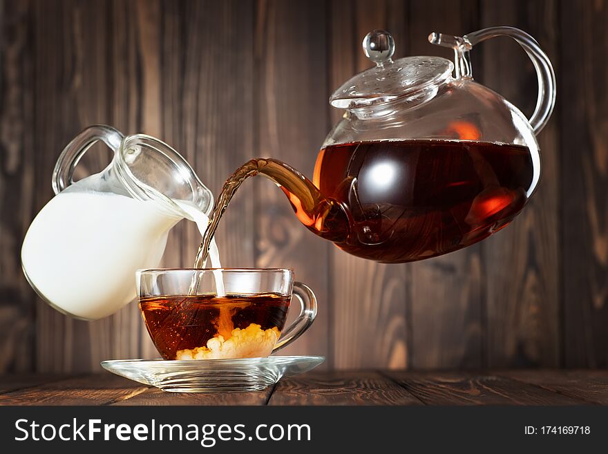 Flying teapot and jug pouring tea with milk into cup on wooden table. Flying teapot and jug pouring tea with milk into cup on wooden table