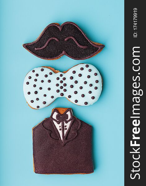 Glazed gingerbread in the form of a mustache, butterfly and tuxedo, men`s set on a blue background. Handmade cookies. Free space. Minimalistic design