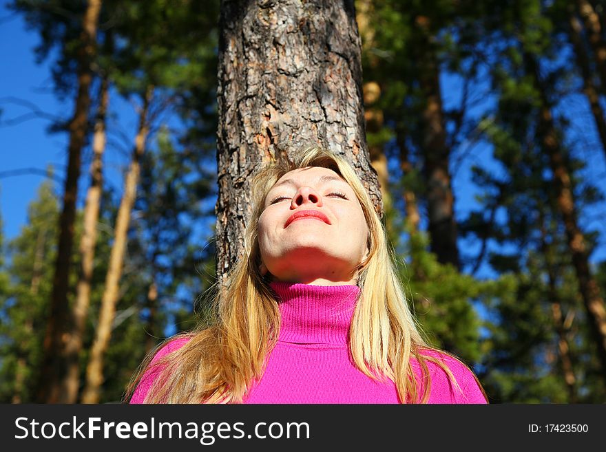 Beauty woman breathes near trunk of pine