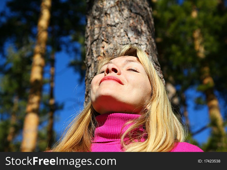 Beauty woman breathes near trunk of pine