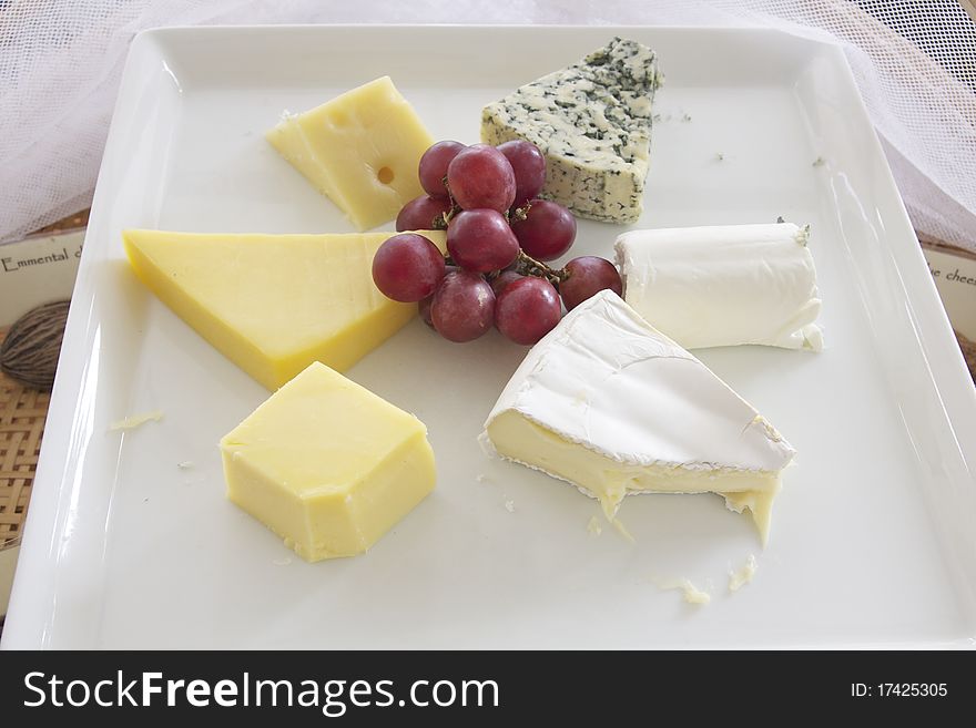 Assorted cheese on plate with a bunch of grape