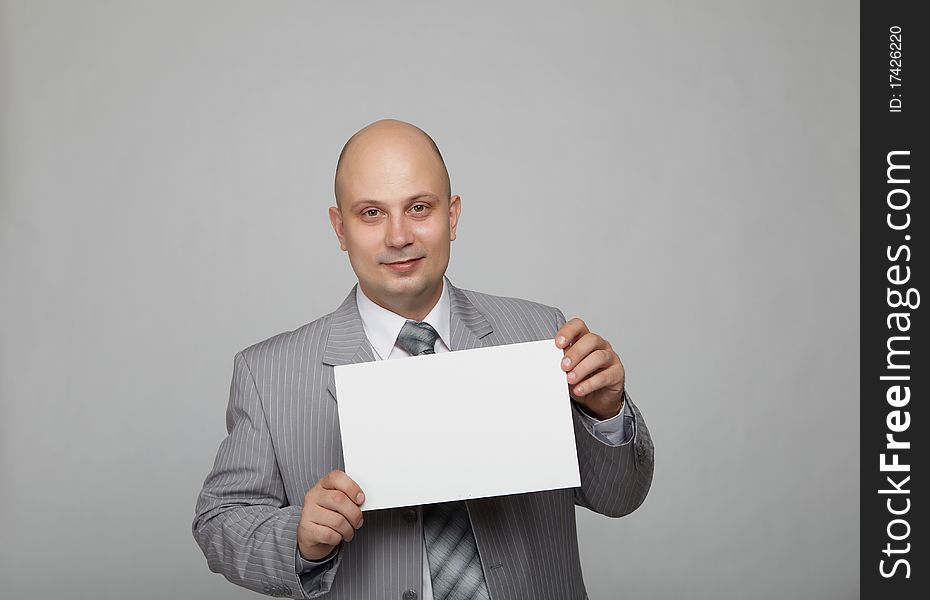 Bald businessman in a gray suit with a gray background with a white square in the hands of