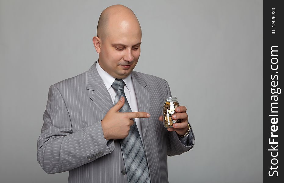 Bald businessman in a gray suit with a gray background with a can with coins in hand